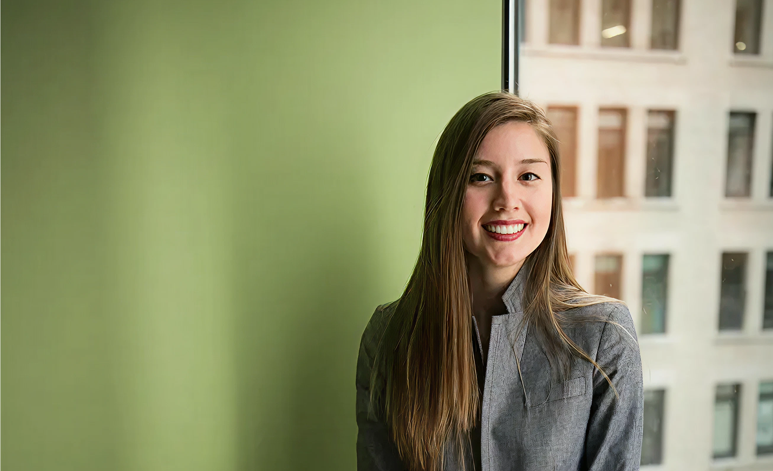 A benefits leader smiling in a bright office with a sage-green wall